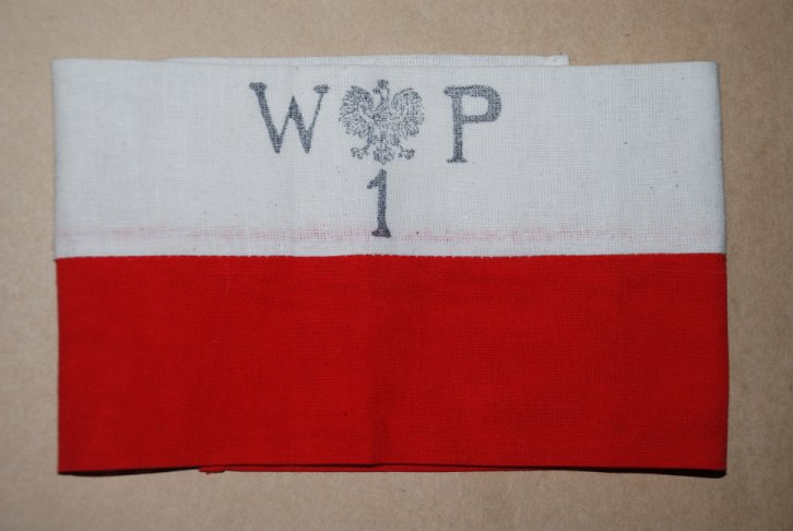 : Armbinde eines Teilnehmenden des Warschauer Aufstandds mit den Buchstaben „WP“ (Abkürzung für „Polnische Armee“). Aus Mangel an Uniformen trugen die Aufständischen solche Armbinden. (© Wikipedia-Benutzer Zuska, CC BY-SA 3.0, abgerufen auf https://commons.wikimedia.org/wiki/File:Opaska_powstancza.jpg)